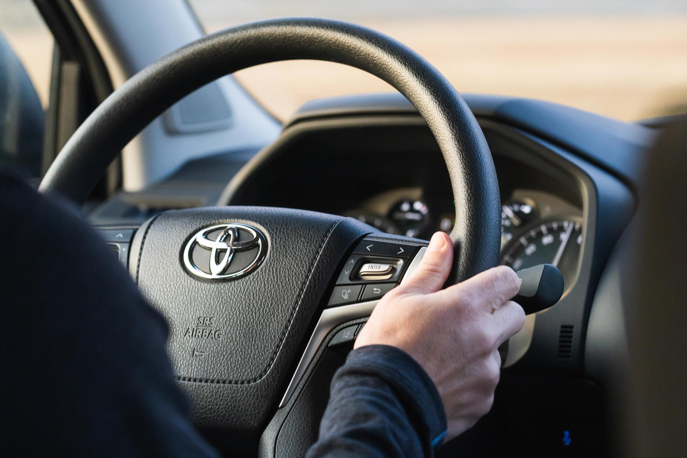 Toyota Land Cruiser steering wheel with a driver's hand on the rim and control buttons