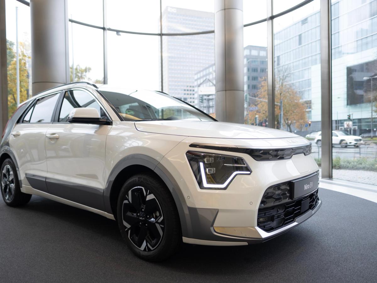 Niro EV séð að framan í sýningarsal Hvítur Kia Niro EV á hringlaga sýningarpalli í sýningarsal með glerveggjum, séður skáhallt að framan