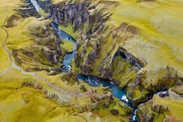 Aerial view of a deep, mossy green canyon with a winding bright blue river.
