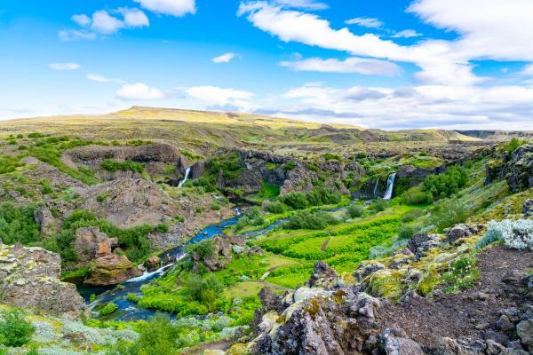 a river flowing through a lush green valley surrounded by rocks and trees .
