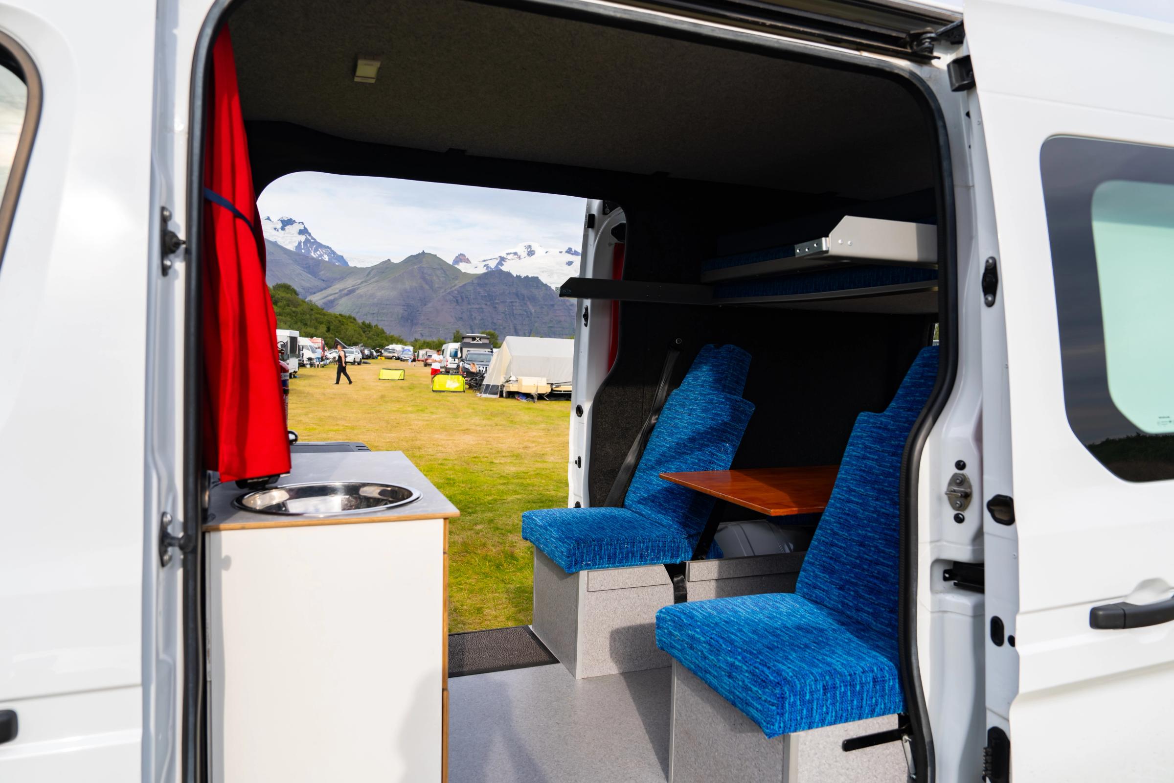 Sink, seats and table with doors open to a campsite in a 5 person large camper
