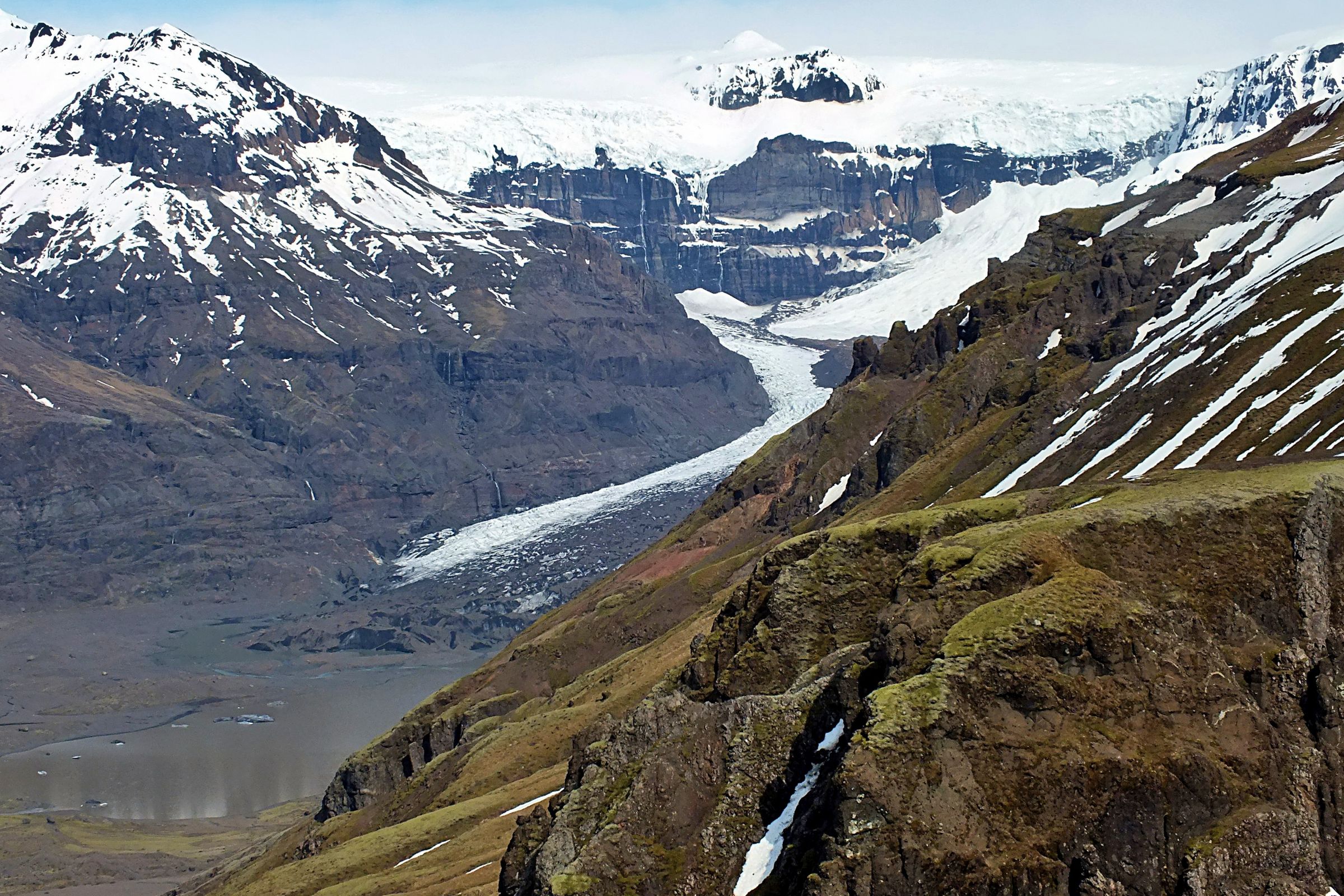 A glacier winds through a valley between snow-capped, rocky mountains.