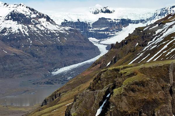 A glacier winds through a valley between snow-capped, rocky mountains.
