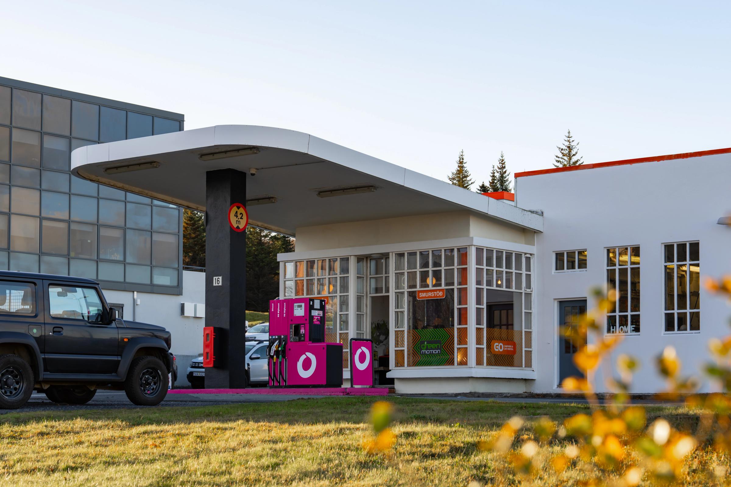 A black SUV at a gas station with bright pink pumps and a white building.