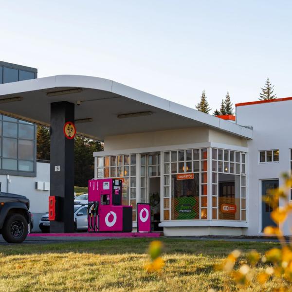A black SUV at a gas station with bright pink pumps and a white building.