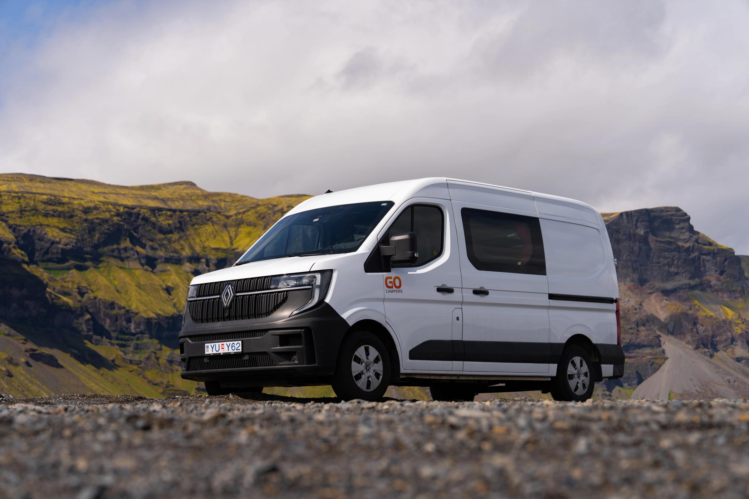 A large camper that sleeps 5 people on gravel ground below rocky cliffs, campervan rental Iceland