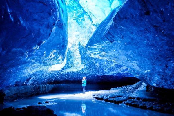 a person is standing in a blue ice cave .