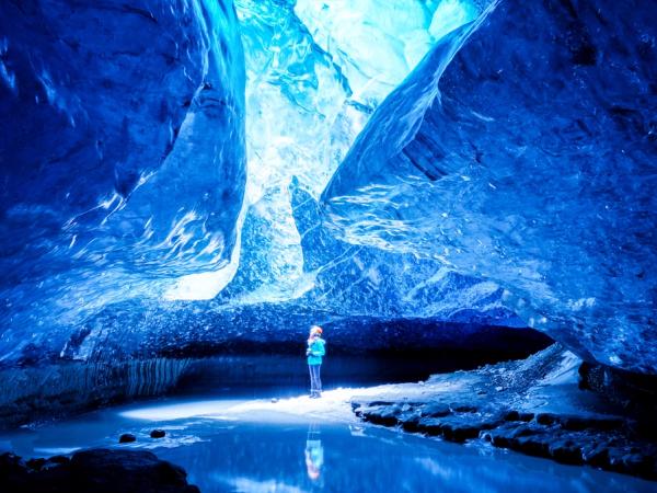 Luminous blue ice cave with a person standing by a pool of water.