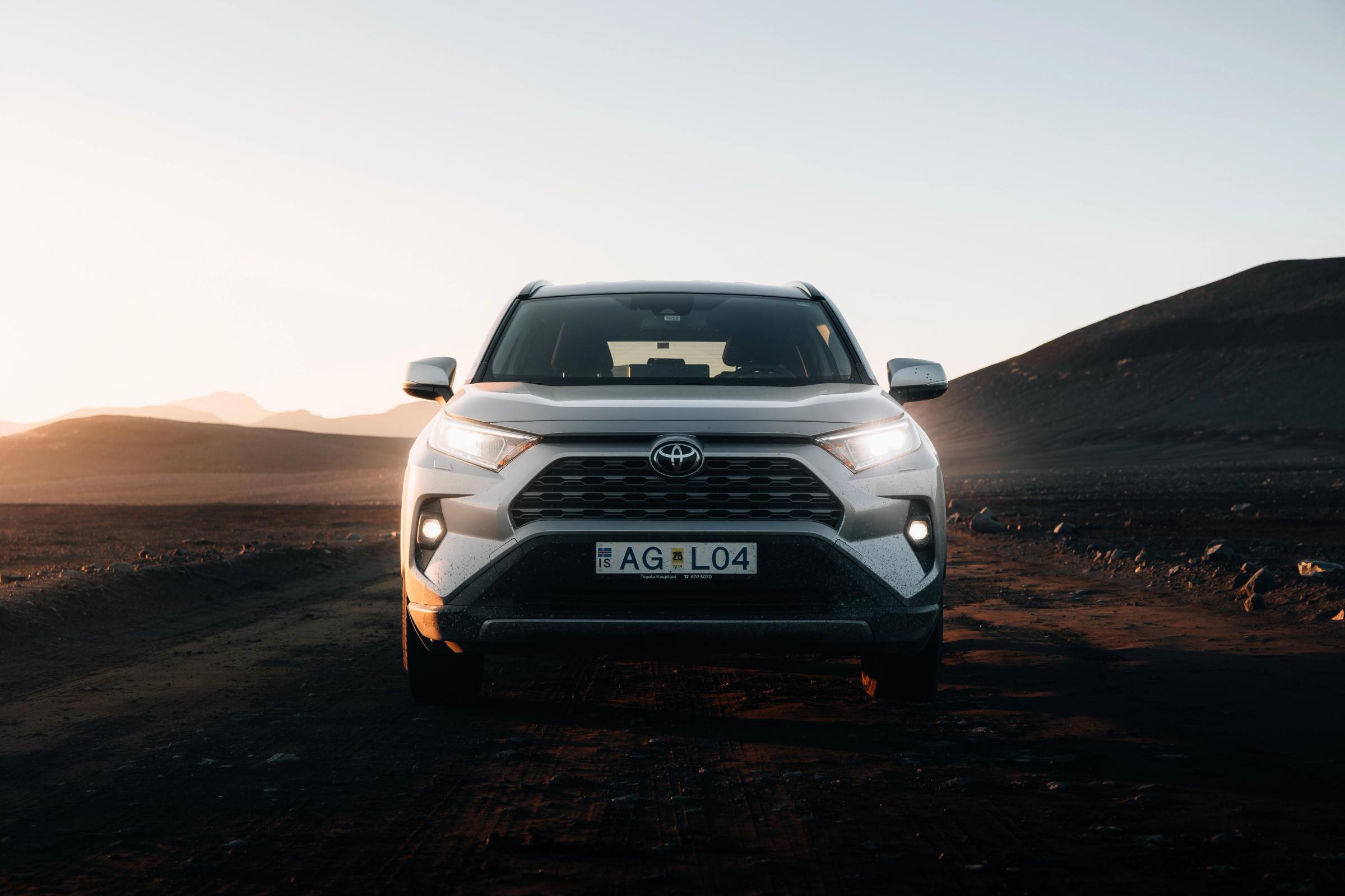Toyota RAV4 seen head on with headlights lit on a gravel track in open landscape