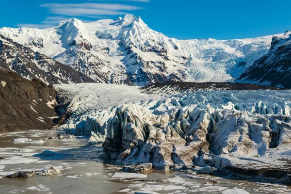 un grand glacier est entouré de montagnes couvertes de neige et d'une rivière .