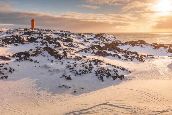 un faro se encuentra en la cima de una colina cubierta de nieve cerca del océano .
