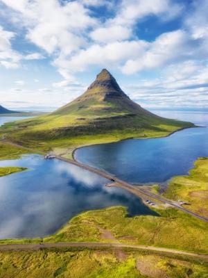 an aerial view of a mountain surrounded by a lake and a road .