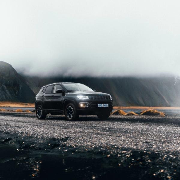 A dark SUV on a gravel road with misty mountains and a cloudy sky in the background.