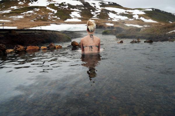 mujer bañándose en Reykjadalur mientras mira una montaña nevada