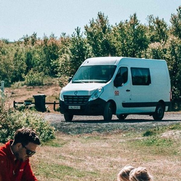 Cámper blanca aparacada al lado de un parque con una familiad en en primer plano