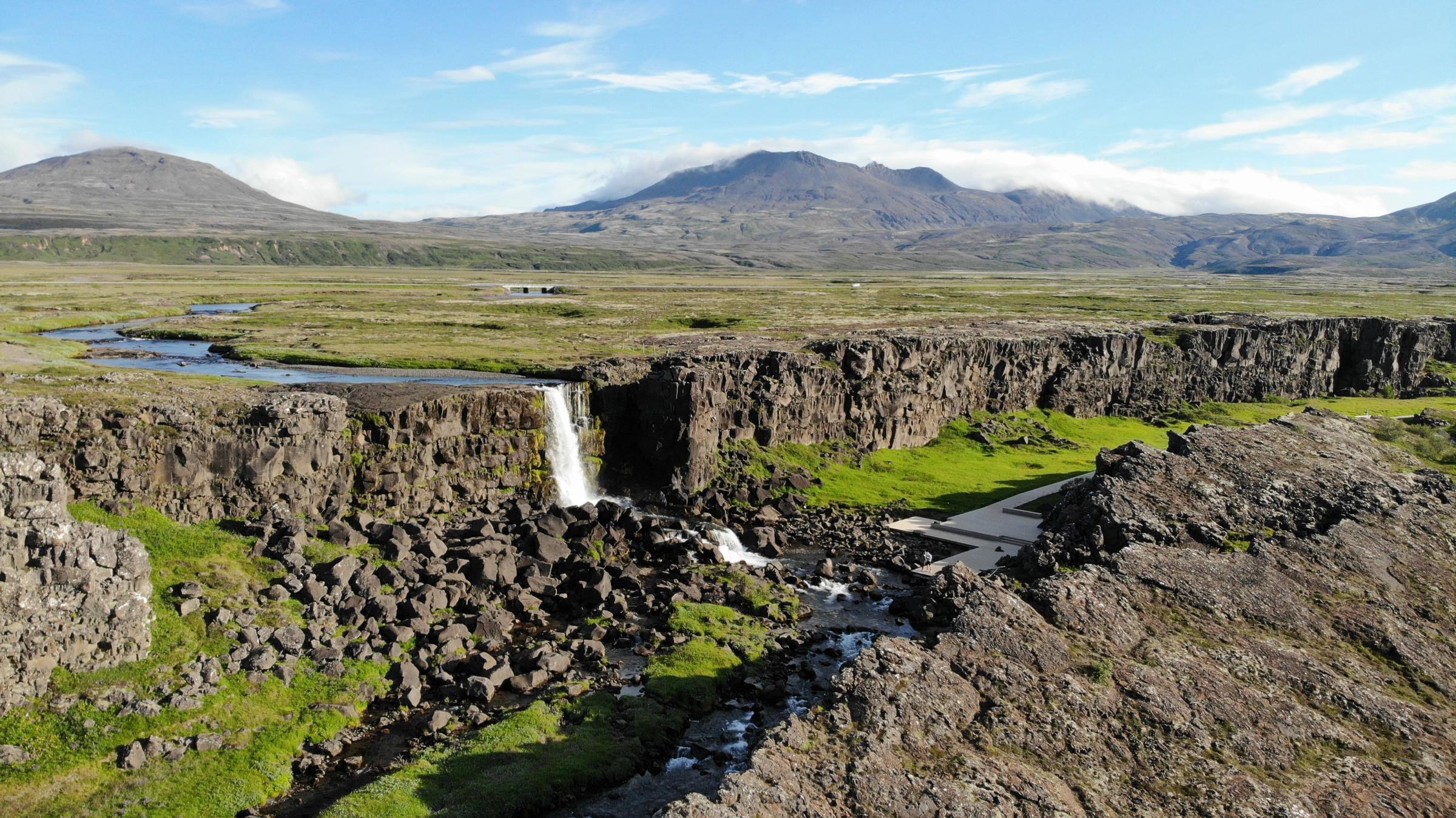an aerial view of a waterfall in the middle of a rocky landscape with mountains in the background .