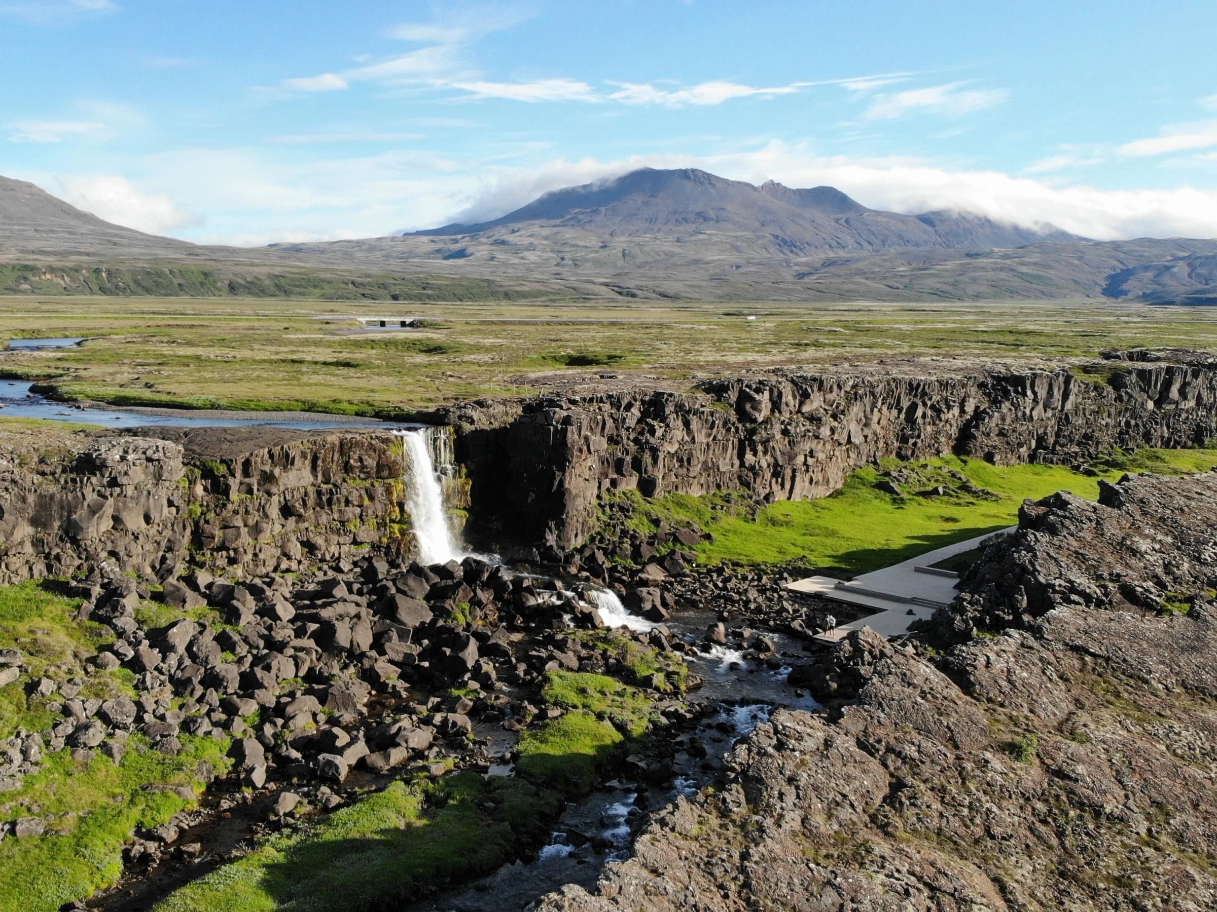 an aerial view of a waterfall in the middle of a rocky landscape with mountains in the background .