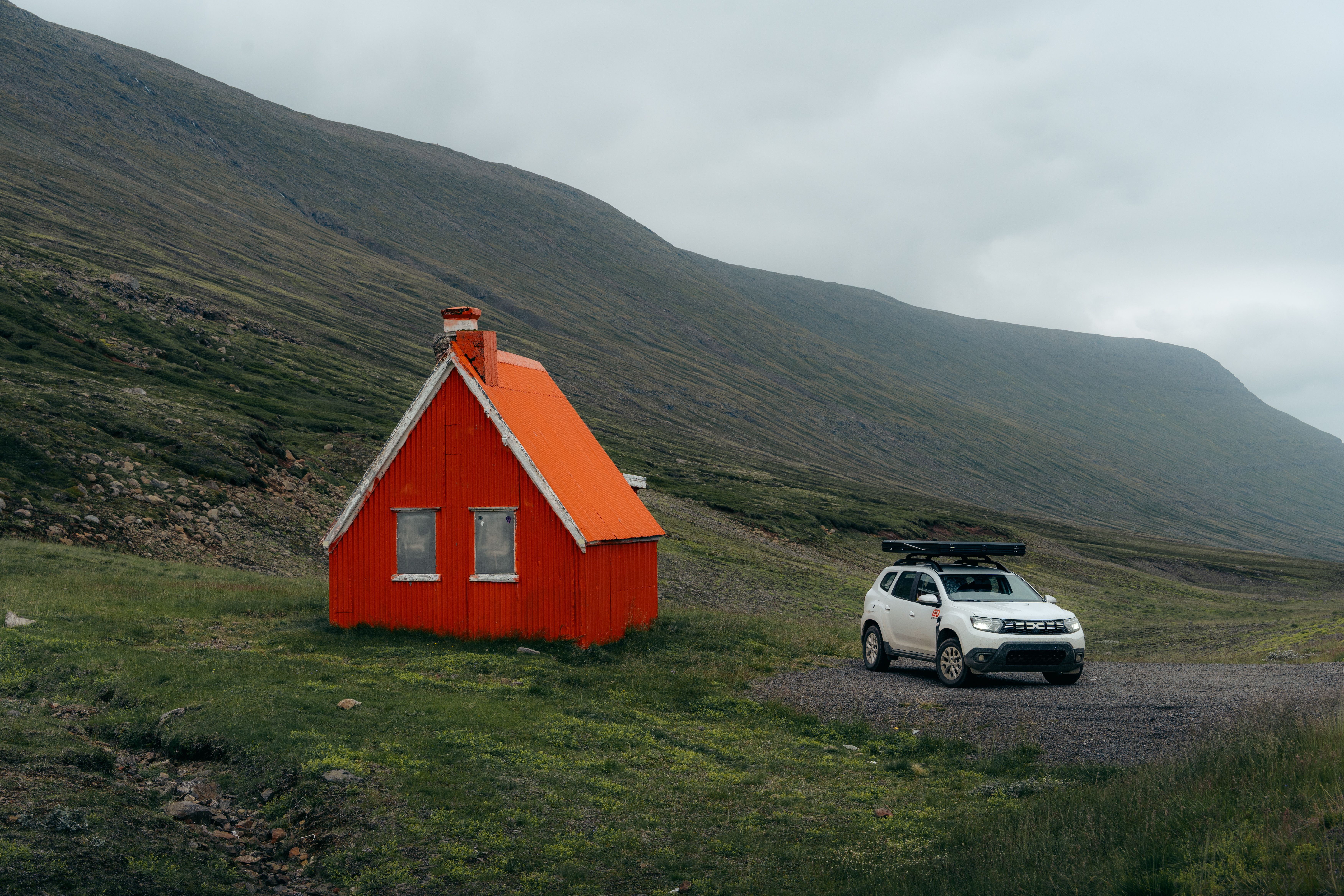 Camper parked on gravel beside a red hut in a mountain valley, 4x4 campervan rental Iceland