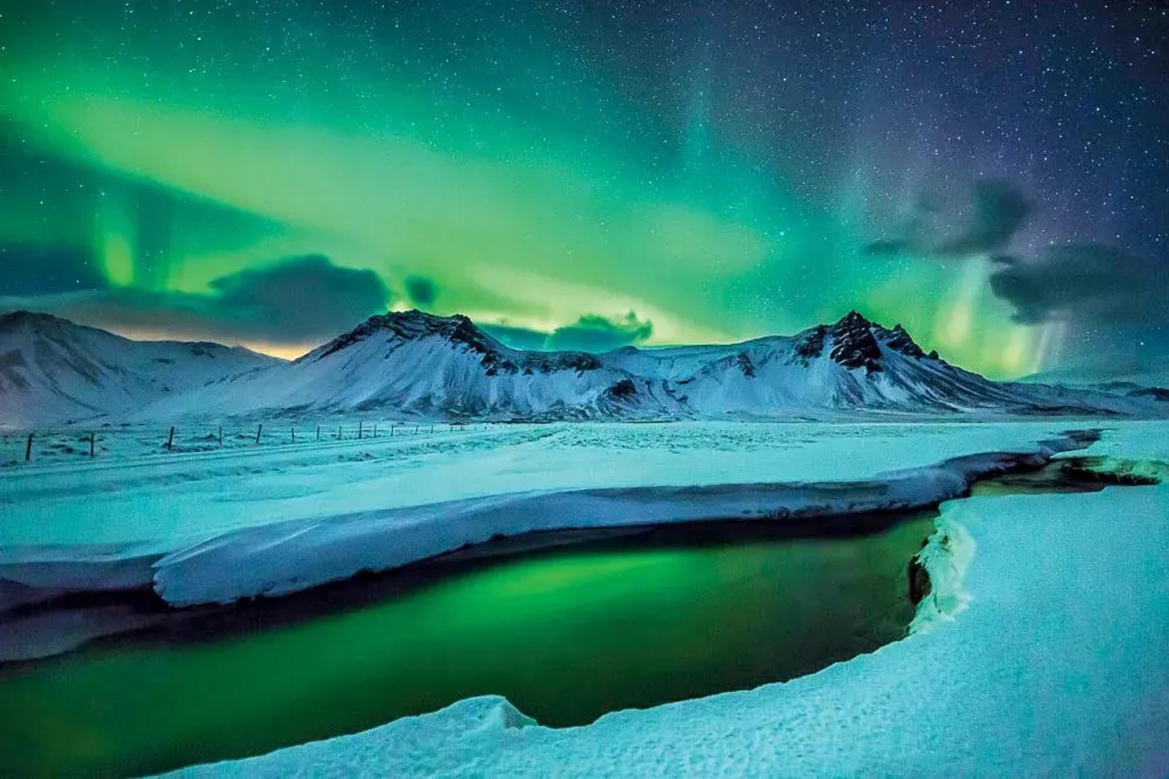 the aurora borealis is shining over a snowy mountain range .
