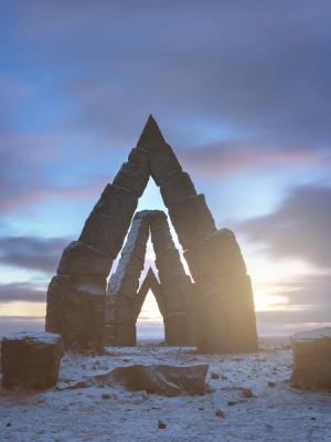 The Arctic Henge in Iceland, with light shining through its stone arches on a snowy plain.