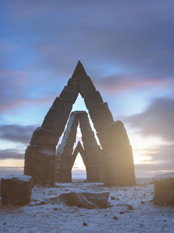 The Arctic Henge in Iceland, with light shining through its stone arches on a snowy plain.