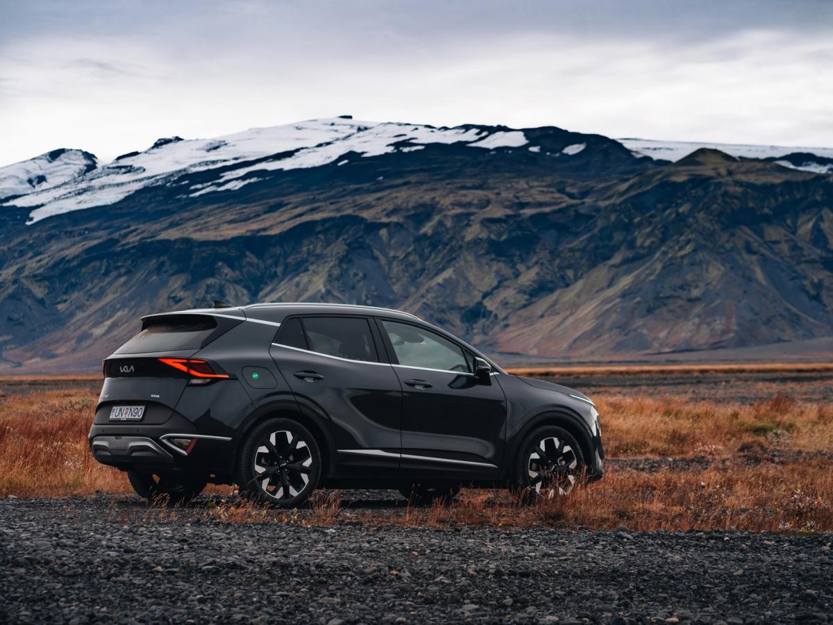 Kia Sportage með fjalllendi í bakgrunni Hliðarmynd af Kia Sportage bílaleigubíl í ferðalagi um Ísland, lagt fyrir neðan fjallshrygg