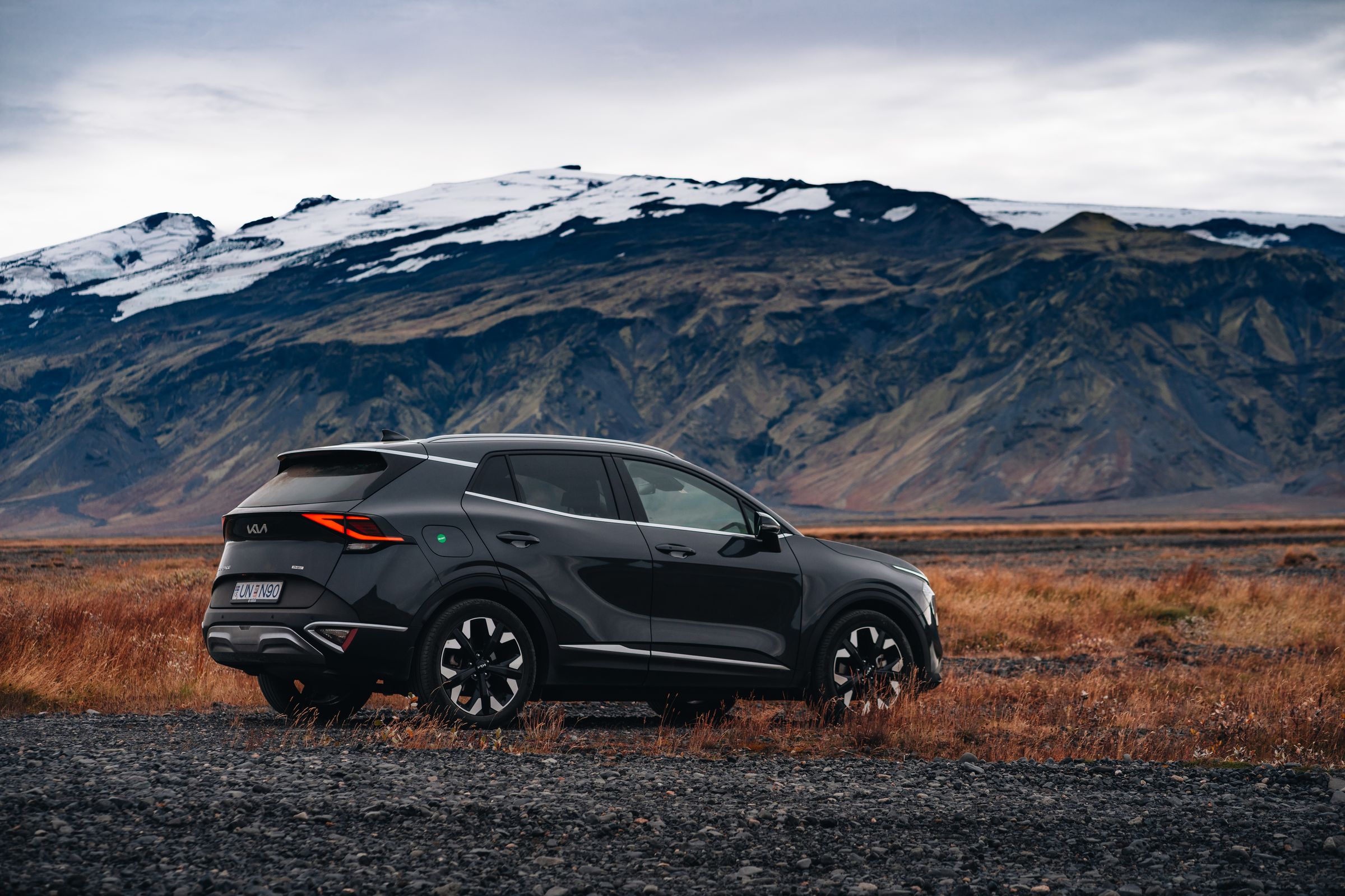 Kia Sportage með fjalllendi í bakgrunni Hliðarmynd af Kia Sportage bílaleigubíl í ferðalagi um Ísland, lagt fyrir neðan fjallshrygg