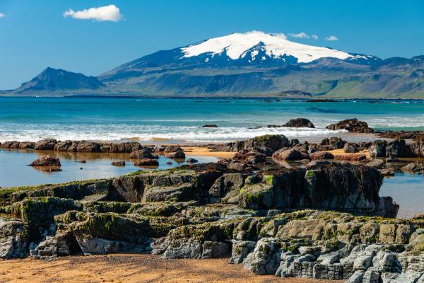 una playa con rocas y una montaña nevada al fondo