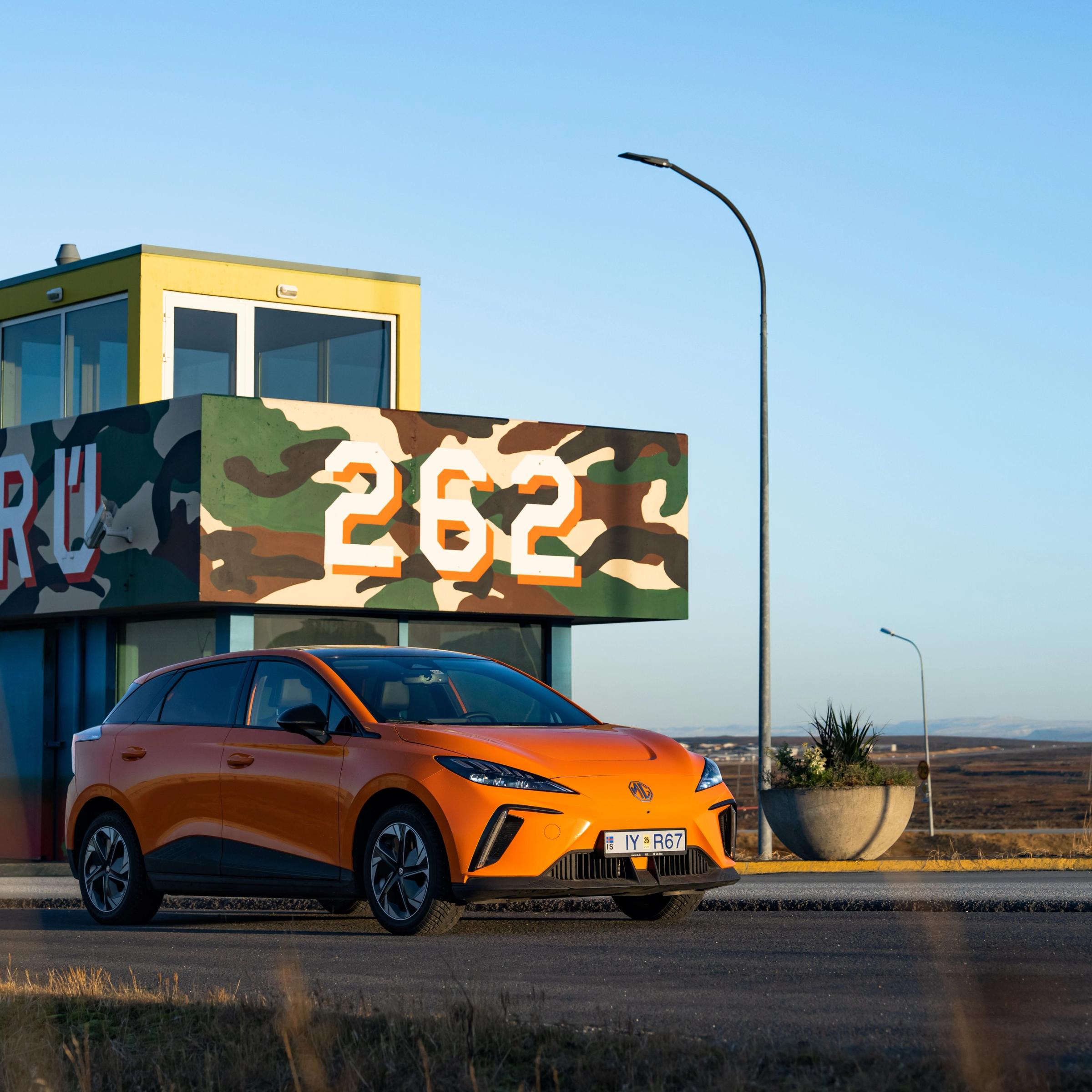 an orange car is parked in front of a camouflage building .