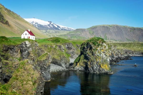 a house over a cliff by the sea with mountains on the background