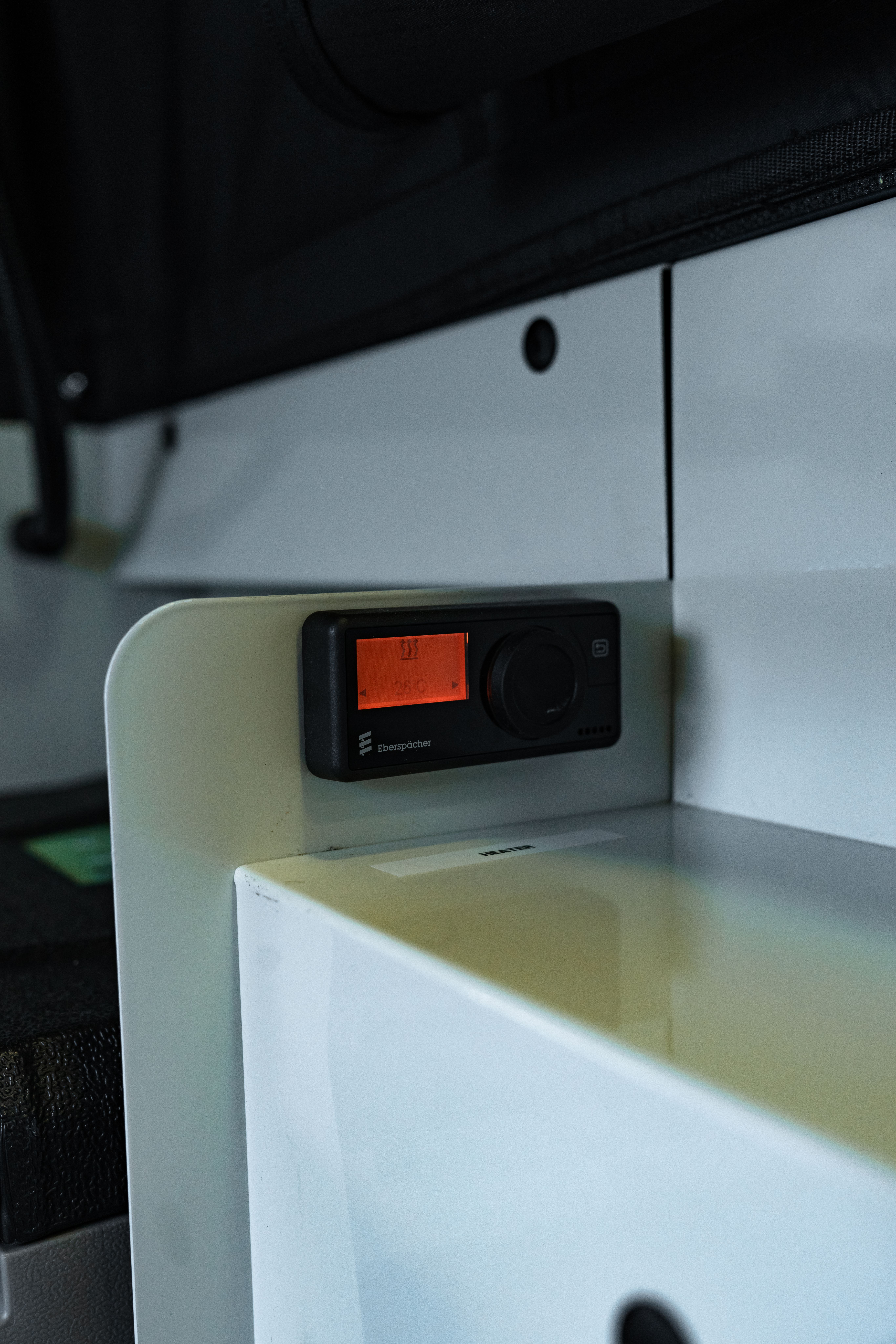 Unidad de control digital de pared con pantalla naranja y mando giratorio, instalada sobre un armario blanco
