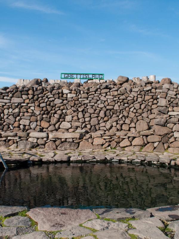 a stone wall surrounds a pool of water surrounded by rocks at Grettislaug hot spring in iceland.