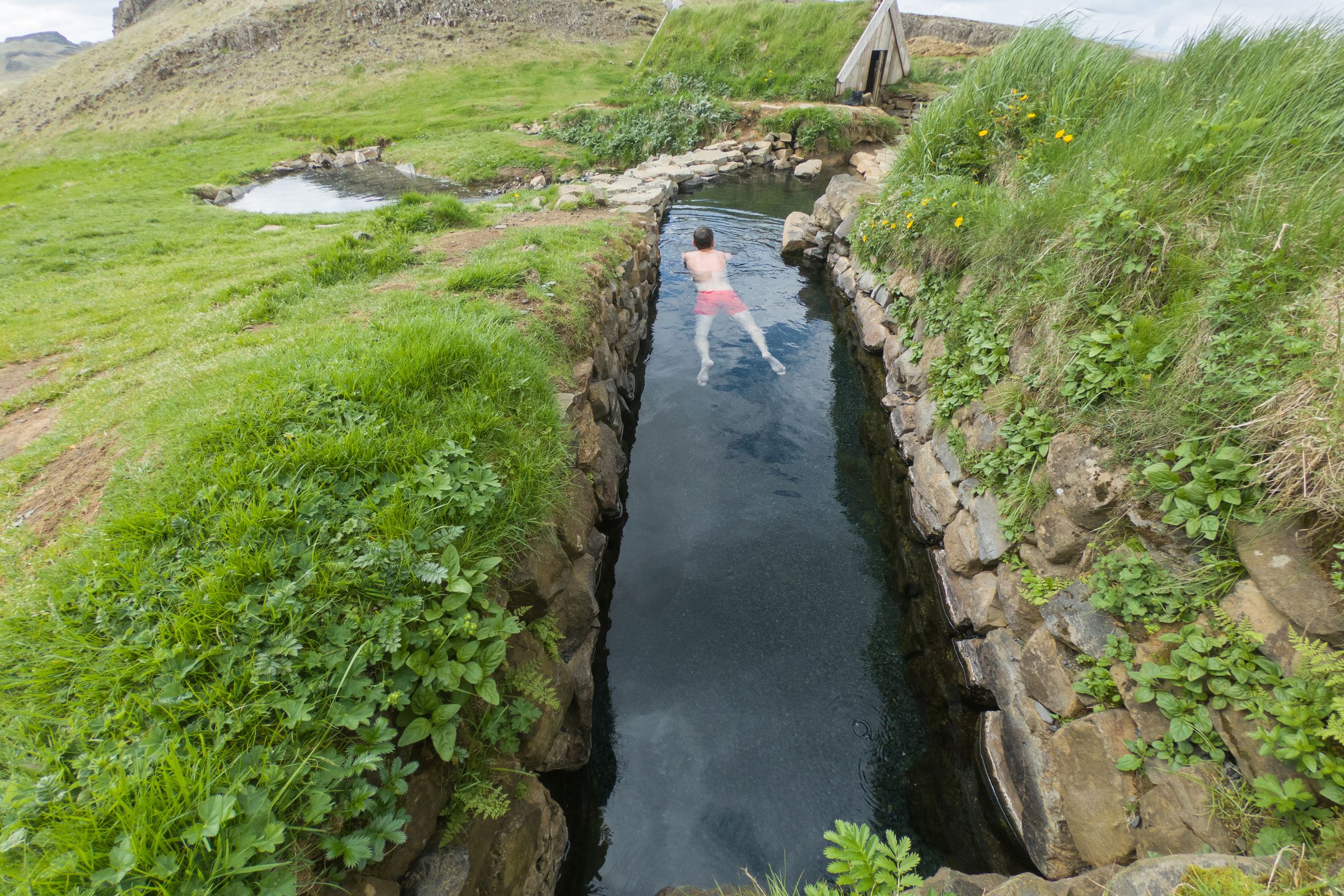 un hombre está nadando en un río rodeado de hierba y rocas.