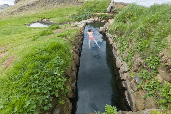 un hombre está nadando en un río rodeado de hierba y rocas.