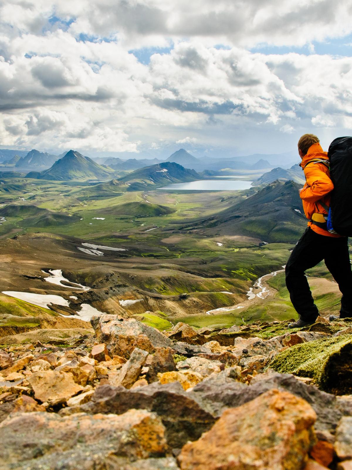 Hiker with a large backpack on a rocky trail overlooking a vast mountain landscape.