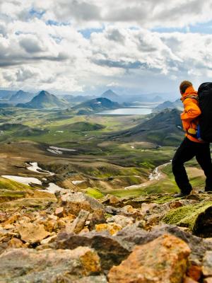 Hiker with a large backpack on a rocky trail overlooking a vast mountain landscape.