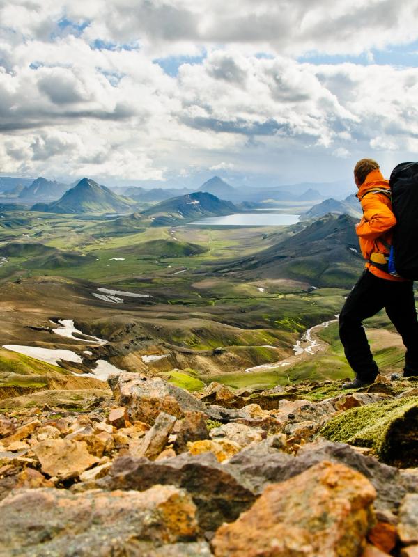 Hiker with a large backpack on a rocky trail overlooking a vast mountain landscape.