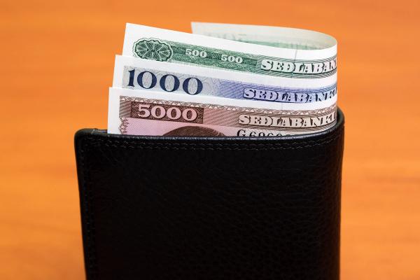 a black wallet filled with Icelandic money on a wooden table .