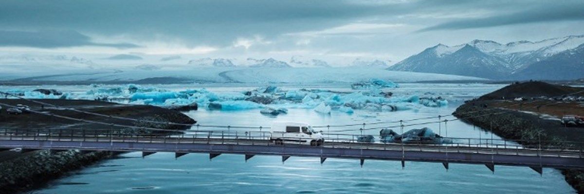 Furgoneta cruzando un puente con una laguna glaciar detrás