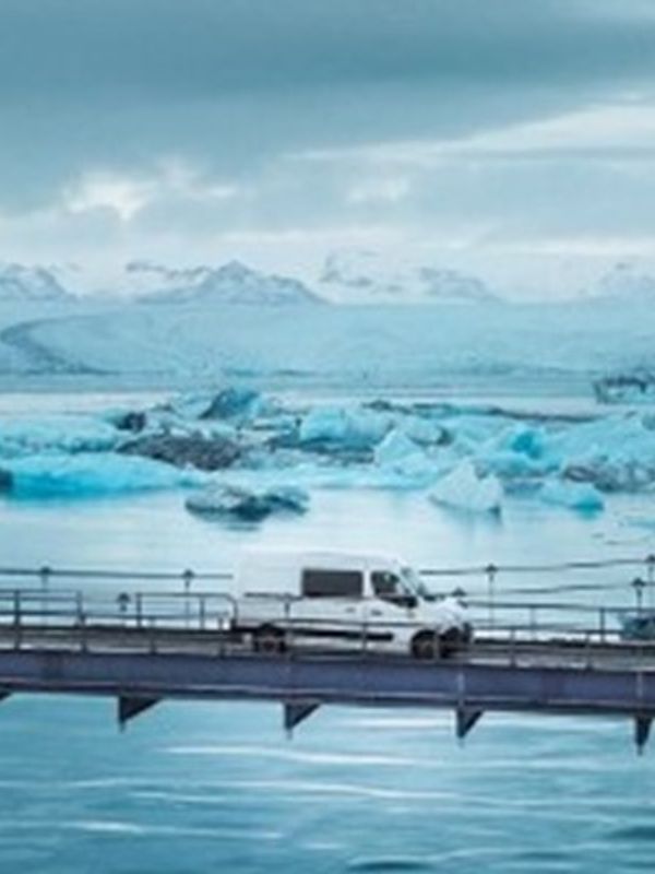 Furgoneta cruzando un puente con una laguna glaciar detrás