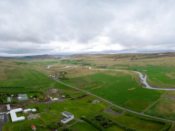 Aerial view of a green valley with a winding river, buildings, and hills under a cloudy sky.