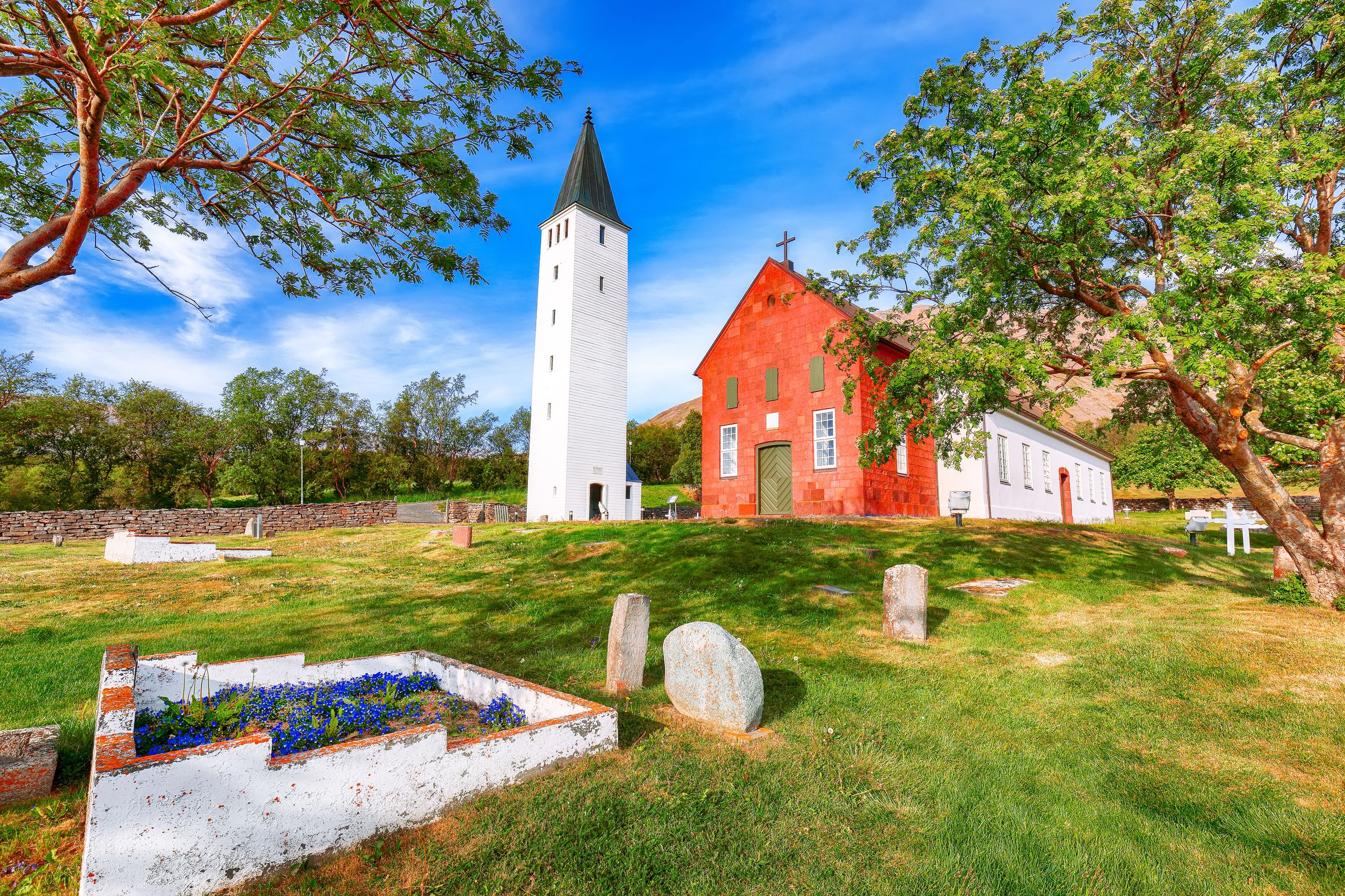 a red church with a white tower and a cemetery in front of it .