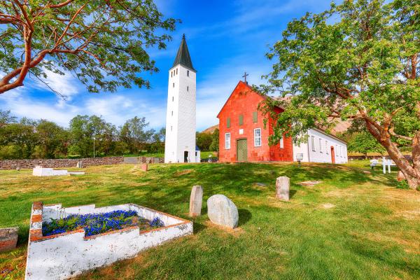 a red church with a white tower and a cemetery in front of it .