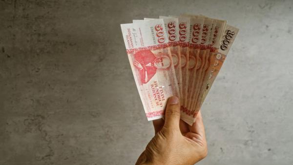 Una mano sosteniendo un abanico de antiguos billetes de rupias indonesias.