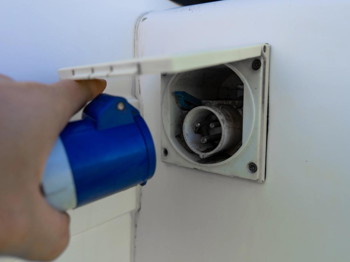 Electric Hookup Inlet Hand connecting a blue hookup cable to the external electrical inlet on the camper