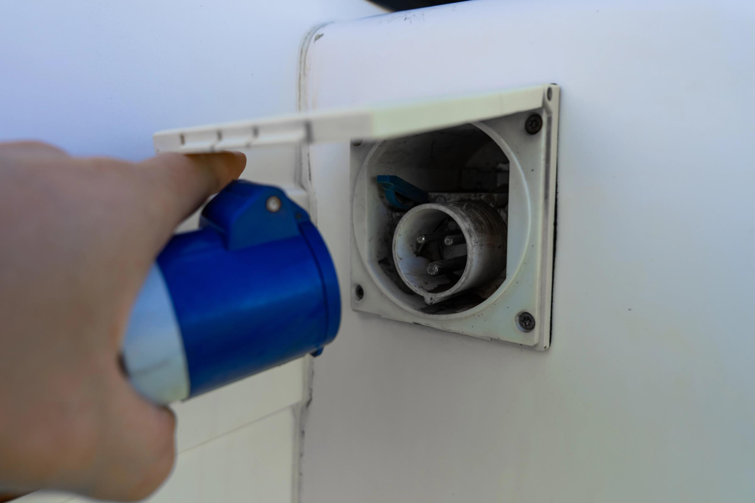 Electric Hookup Inlet Hand connecting a blue hookup cable to the external electrical inlet on the camper