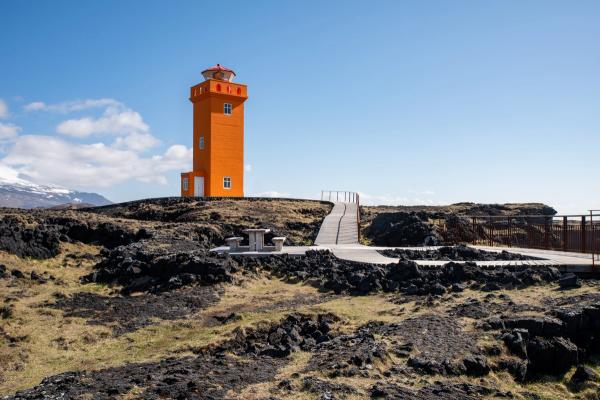 un faro naranja se encuentra en la cima de una colina rocosa .