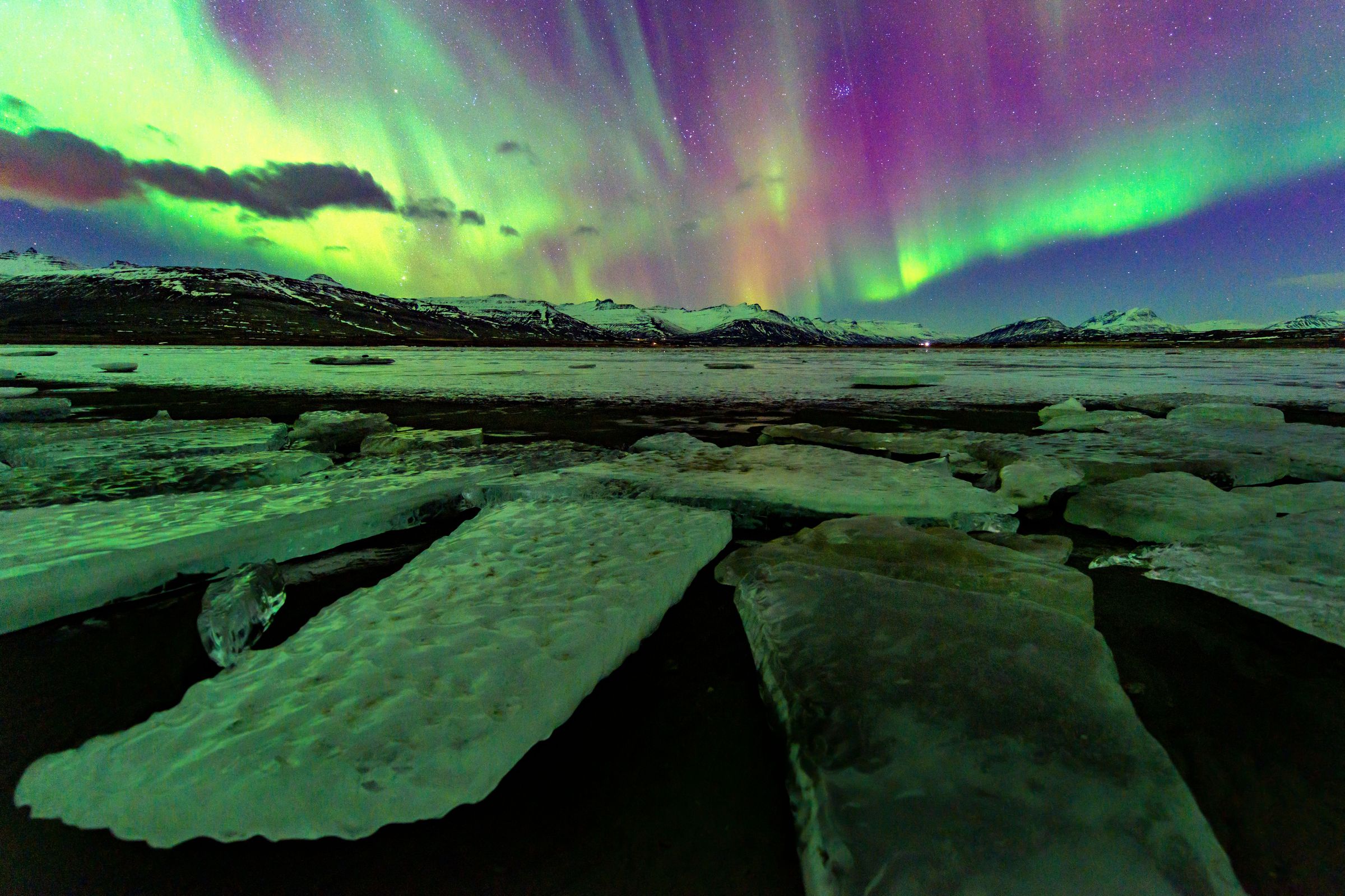 the aurora borealis is shining over a frozen lake .