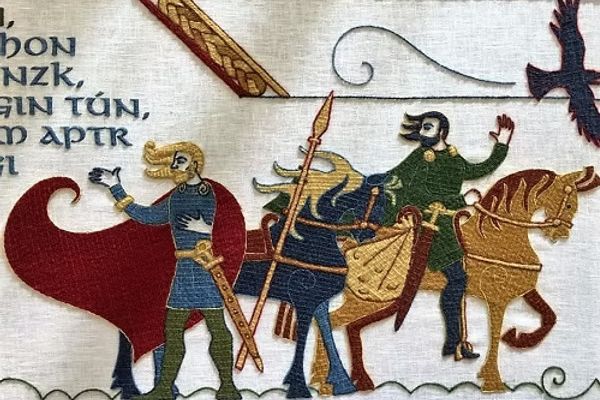 Embroidered tapestry in Bayeux Tapestry style showing a blond man in a red cloak gesturing, a man on horseback waving, and a raven.