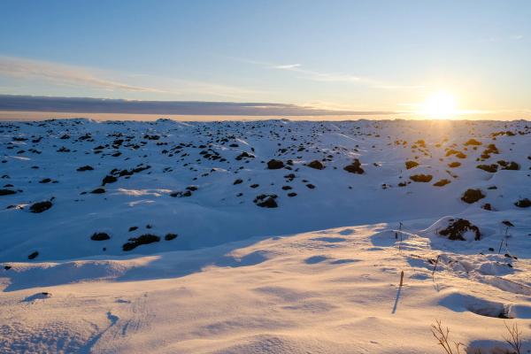 Snowy, rugged landscape with a brilliant sun low on the right horizon.